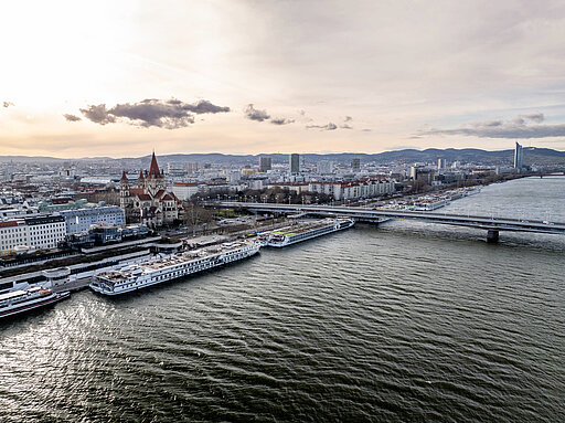 Luftaufnahme der Donau in Wien mit angelegten Kreuzfahrtschiffen und Stadtansicht nahe der Reichsbrücke.
